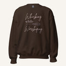 Brown crewneck sweatshirt with "Whisking while Worshiping" pink text with a pink whisk graphic.