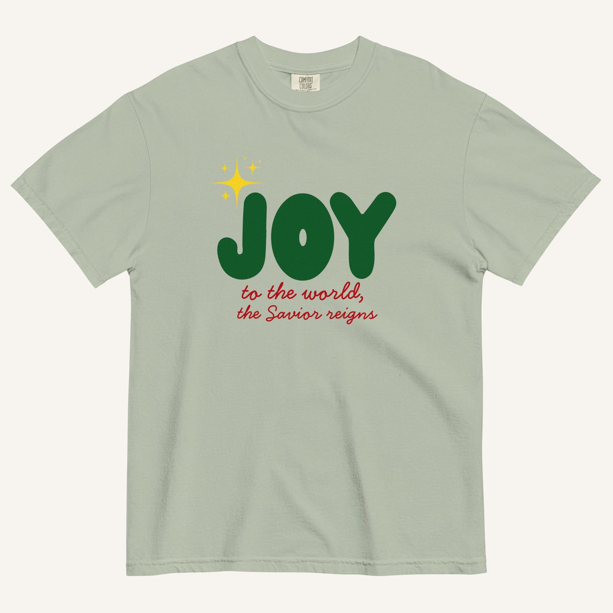 a muted sage green t-shirt with the words "Joy to the world, the Savior reigns" in bold colorful font with a star graphic