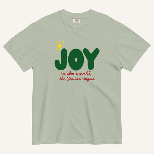 a muted sage green t-shirt with the words "Joy to the world, the Savior reigns" in bold colorful font with a star graphic