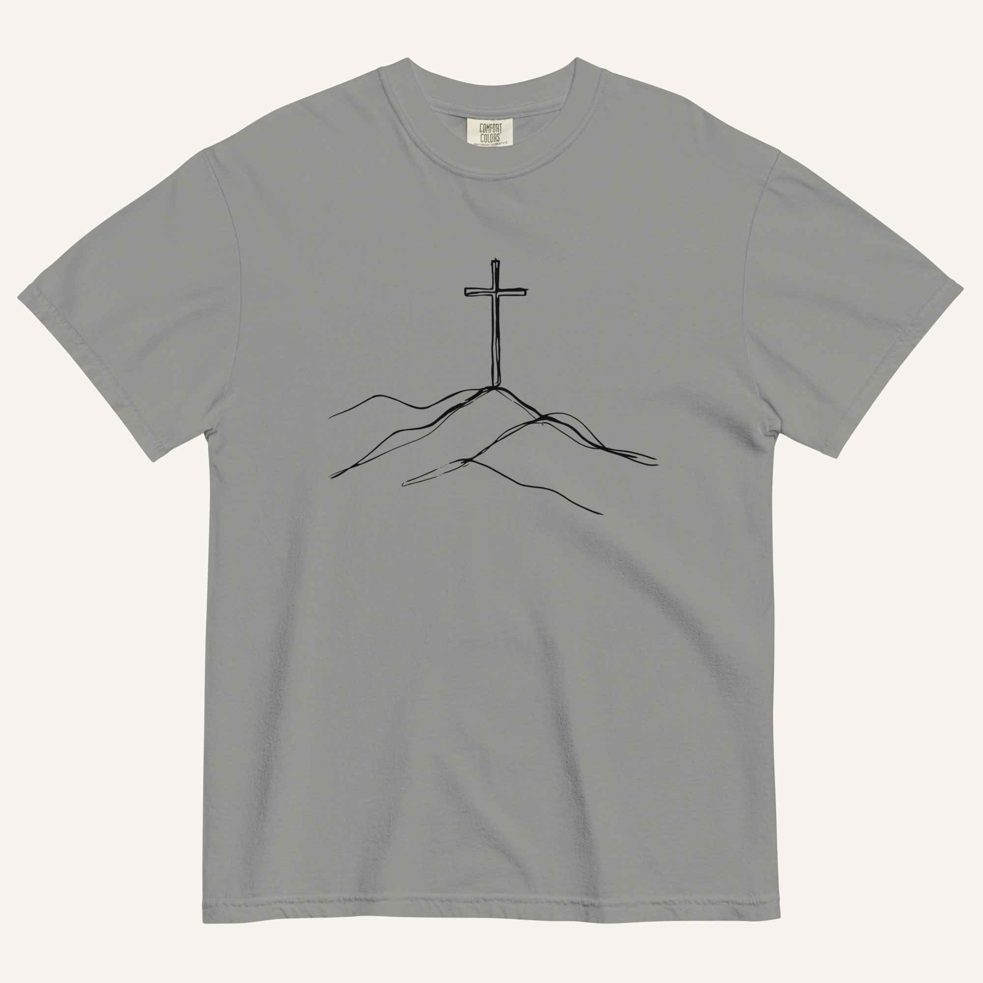 A gray short-sleeve crewneck t-shirt featuring a minimalist black line art graphic of a cross rising from simple hills on the chest, displayed flat against a light off-white background.