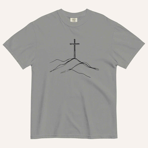 A gray short-sleeve crewneck t-shirt featuring a minimalist black line art graphic of a cross rising from simple hills on the chest, displayed flat against a light off-white background.
