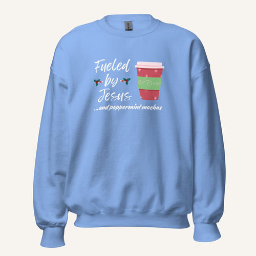 Light blue unisex crewneck sweatshirt featuring a Christmas design with the phrase “Fueled by Jesus …and peppermint mochas,” peppermint illustrations, and a festive red and green peppermint mocha cup graphic.