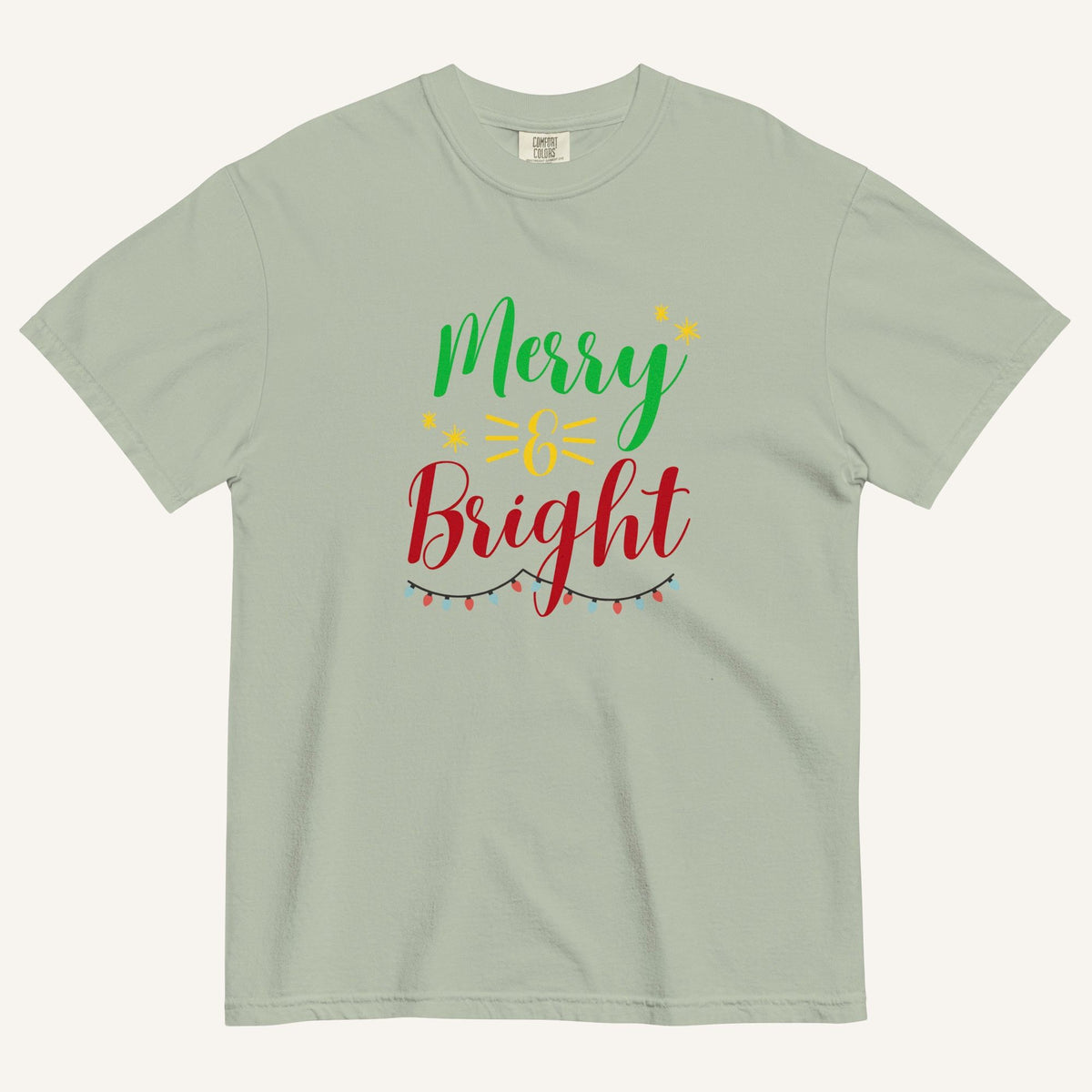 a muted sage green t-shirt that has "Merry & Bright" colored text with Christmas lights and star graphics