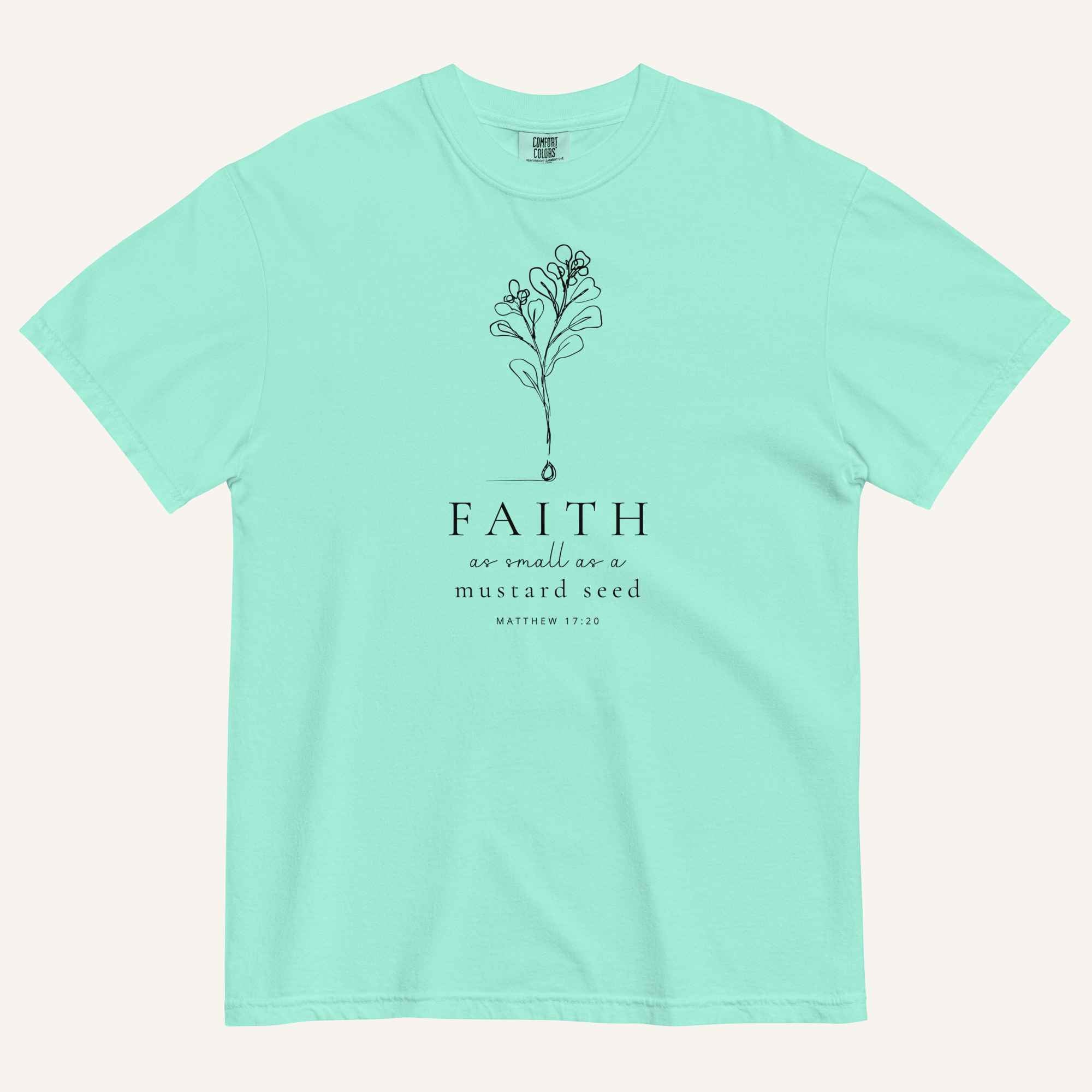 A  mint green short-sleeve crewneck t-shirt with a black line-art mustard seed graphic and the text 'FAITH as small as a mustard seed' and 'MATTHEW 17:20' printed on the front, displayed against a light cream background.