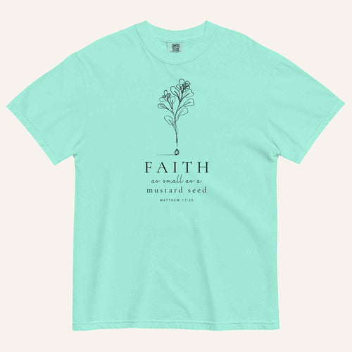A  mint green short-sleeve crewneck t-shirt with a black line-art mustard seed graphic and the text 'FAITH as small as a mustard seed' and 'MATTHEW 17:20' printed on the front, displayed against a light cream background.