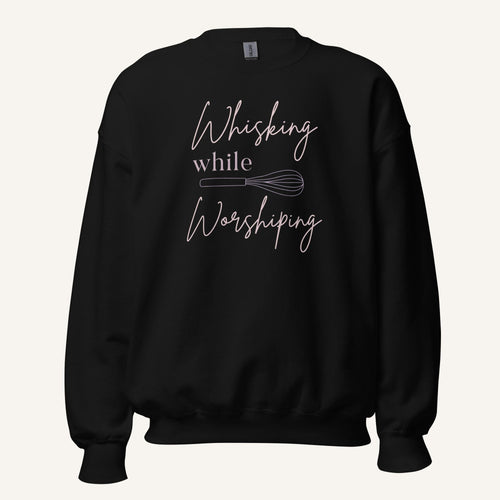 Black crewneck sweatshirt with "Whisking while Worshiping" pink text with a pink whisk graphic.