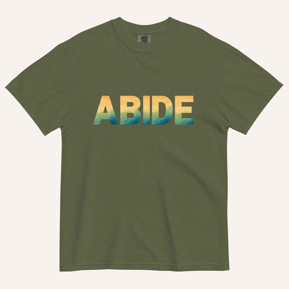 A dark green crewneck t-shirt featuring the word 'ABIDE' printed across the chest in a bold sans-serif font with a yellow-to-blue gradient.