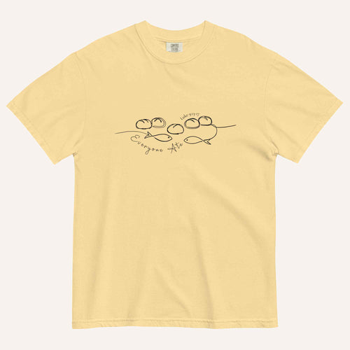 A yellow short-sleeve crewneck t-shirt with a black graphic of two fish and 5 loaves of bread on a line and the cursive text 'Everyone Ate' across the chest, displayed flat against a light beige background.