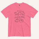 A bright pink short-sleeve t-shirt with a black graphic print on the front showing fish and loaves of bread, with the text 'He Provides' and 'Matthew 14:13-21'.
