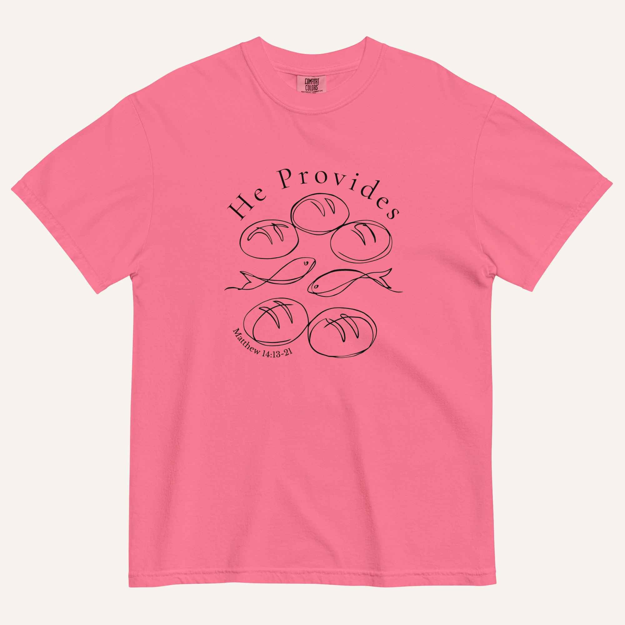 A bright pink short-sleeve t-shirt with a black graphic print on the front showing fish and loaves of bread, with the text 'He Provides' and 'Matthew 14:13-21'.
