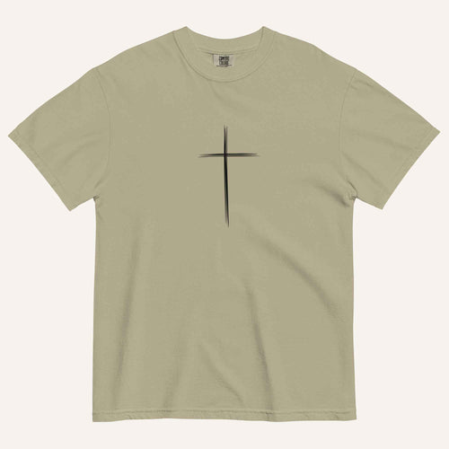 A short-sleeve crewneck t-shirt in a light olive green color, featuring a simple black Christian cross printed on the center chest. The t-shirt is laid flat against a solid, warm off-white background.