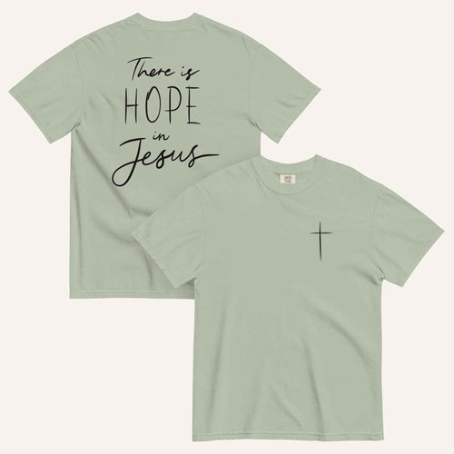 A sage green t-shirt shown from both the front and back. The front features a small black cross on the top left. The back features the black text 'There is HOPE in Jesus' in a mix of script and block lettering.