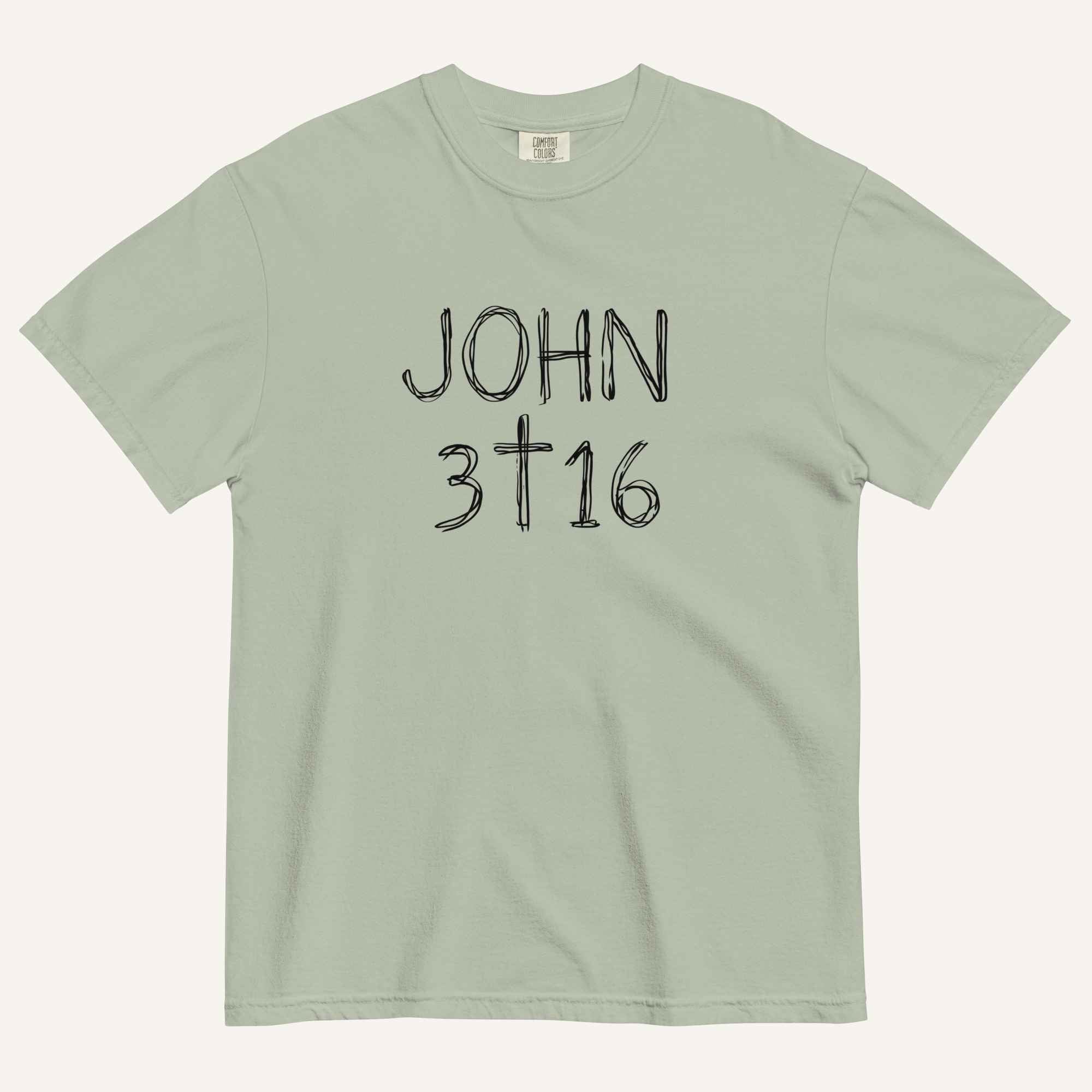 A sage green short-sleeve crewneck t-shirt with 'JOHN 3 16' text with cross graphic in between the 3 & 16 printed in a black hand-drawn font on the chest, displayed flat against a light cream background.