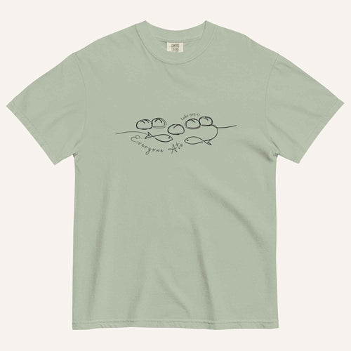 A sage green short-sleeve crewneck t-shirt with a black graphic of two fish and 5 loaves of bread on a line and the cursive text 'Everyone Ate' across the chest, displayed flat against a light beige background.