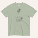 A sage green short-sleeve crewneck t-shirt with a black line-art mustard seed graphic and the text 'FAITH as small as a mustard seed' and 'MATTHEW 17:20' printed on the front, displayed against a light cream background.