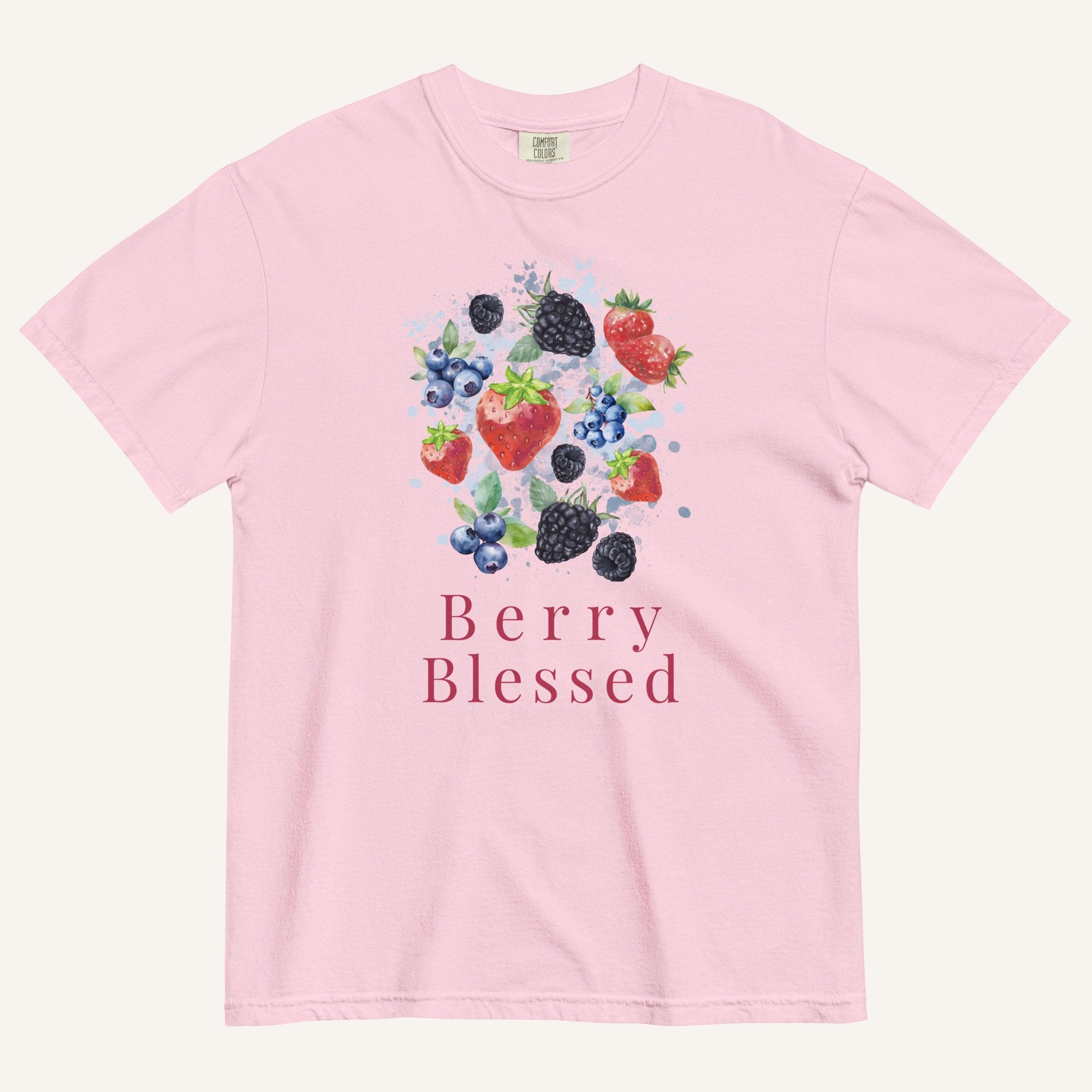 A light pink short-sleeve crewneck t-shirt featuring a colorful watercolor graphic of various berries (strawberries, blueberries, blackberries) and the text 'Berry Blessed' printed below it, displayed on a clean off-white background.