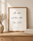 Framed print with 'Be still and know that I am God' on a wooden surface with decor items.