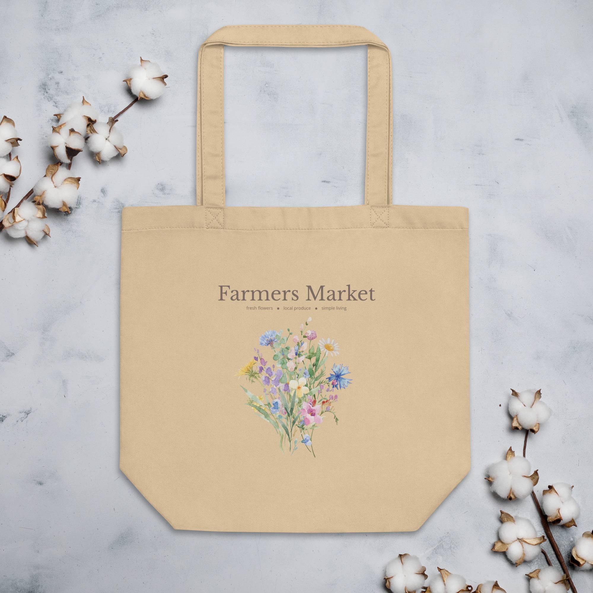 Beige tote bag with floral design and 'Farmers Market' text on a light gray background with cotton branches.
