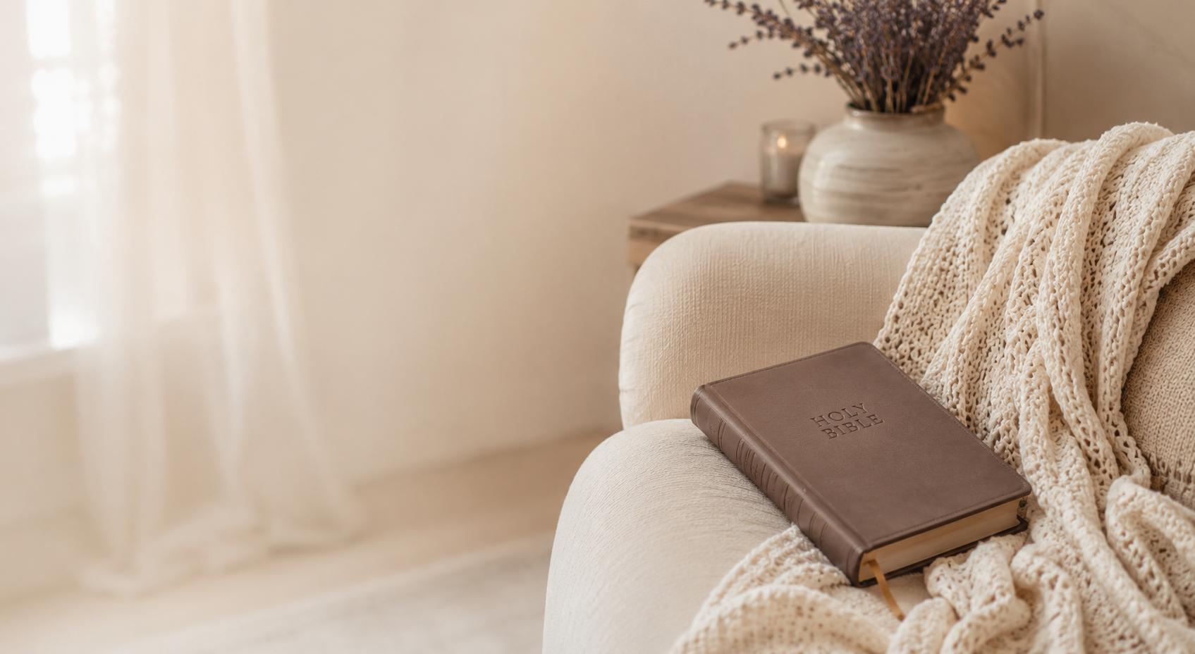 Brown leather-bound book on a white armchair with a soft blanket and decorative elements in a cozy room.