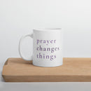 White mug with 'prayer changes things' text on a wooden surface