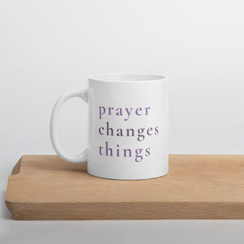 White mug with 'prayer changes things' text on a wooden surface