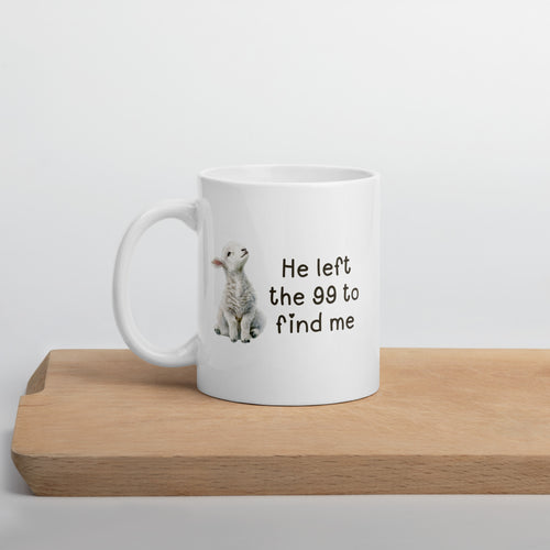 white 11 oz mug with a watercolor lamb and 'He left the 99 to find me' text sitting on a wooden board